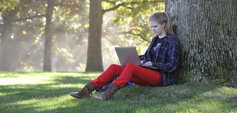 student sitting under a tree with her laptop